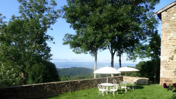 Ein Gebäude aus Stein mit einer Steinsäule, weißen Gartenmöbeln und Sonnenschirmen.
