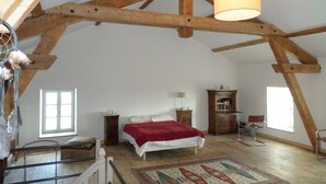 Ein Schlafzimmer mit Holzboden, einem Bett mit roter Decke, einem Schminktisch, einem Stuhl und einem Fenster.