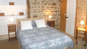 Une chambre à coucher avec un lit, deux tables de chevet avec des lampes, une porte en bois et un mur en pierre.
