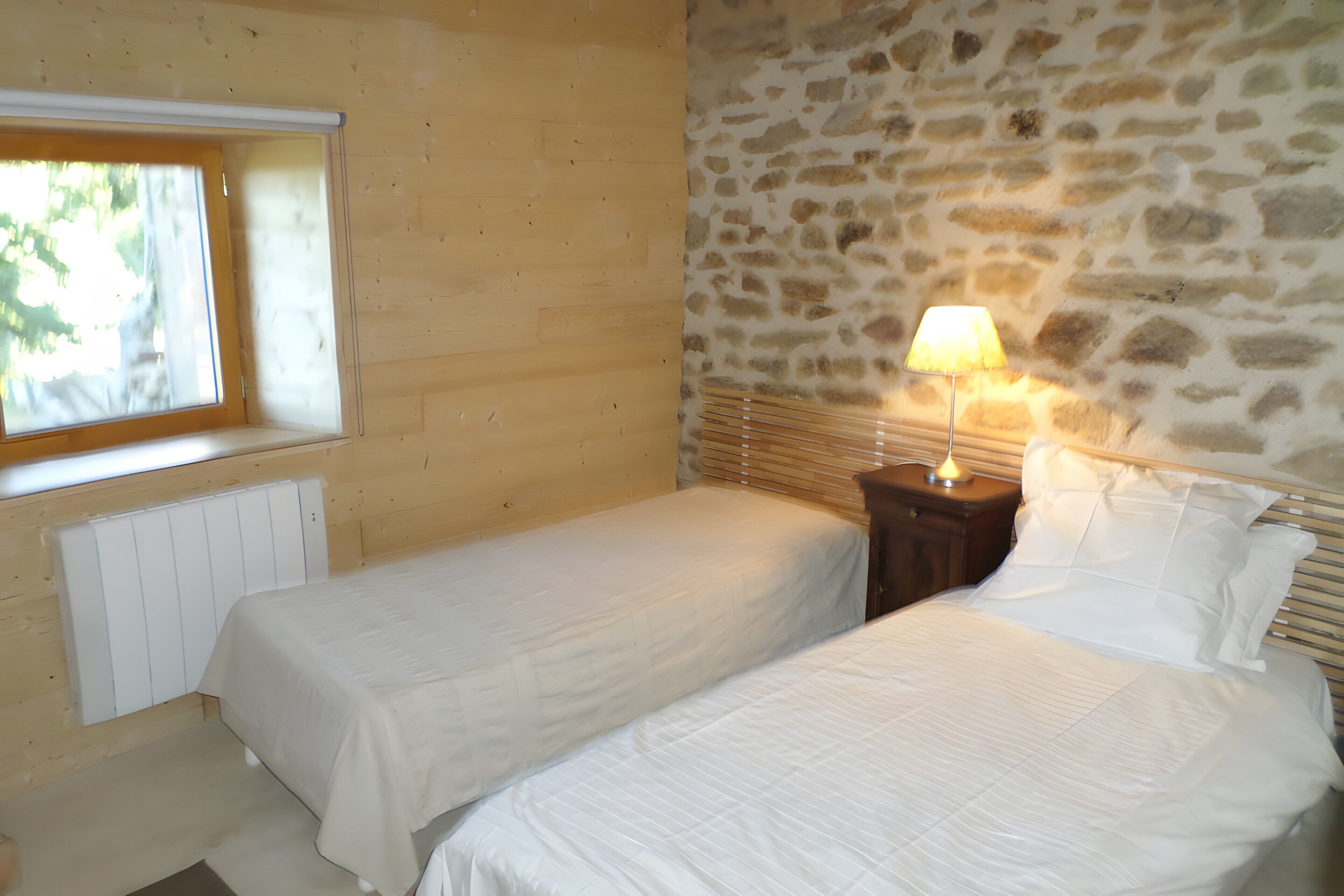 Ein Schlafzimmer mit zwei Betten, einer Steinsäule, einem Fenster und einem Nachttisch mit Lampe.