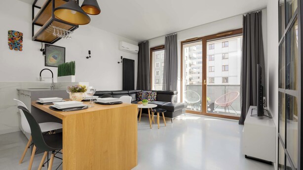 Eine moderne Wohnung mit Küche, Essbereich und Wohnzimmer. Sie verfügt über ein großes Fenster, einen Flachbildfernseher und einen Balkon mit einem Stuhl.