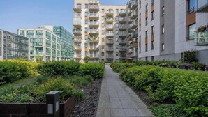 Ein modernes Apartmenthaus mit einem zentralen Innenhof, umgeben von Grünflächen und einem gepflasterten Weg.