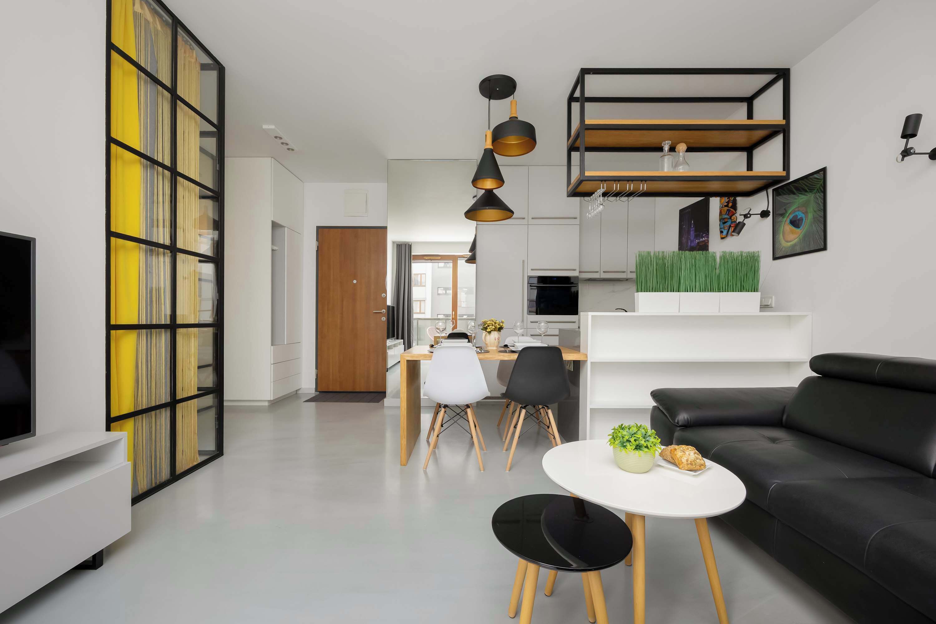 A modern living room with a black sofa, a white coffee table, and a dining area with a white table and chairs.