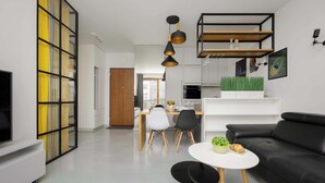 Ein modernes Wohnzimmer mit einem schwarzen Sofa, einem weißen Couchtisch und einem Essbereich mit weißem Tisch und Stühlen.