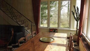 Ein Essbereich mit Holztisch, Stühlen, einem dekorativen Metallgeländer und Blick auf Bäume durch große Fenster.
