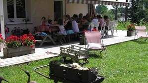 Ein Essbereich im Freien mit Tischen, Stühlen, einem Grill und Kübelpflanzen.