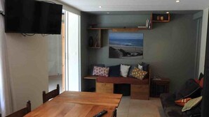 Ein Wohnzimmer mit einem Holztisch, einer Couch, einem an der Wand montierten Fernseher und einem Gemälde über der Couch.