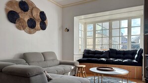 En stue med en grå sofa, en sort sofa, et rundt sofabord og et stort kunstværk på væggen.