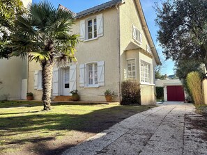 Une maison à deux étages avec des volets blancs, une porte de garage rouge et une allée gravillonnée.