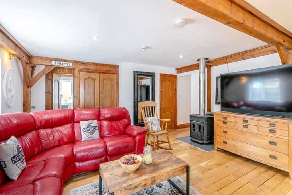 Un salon chaleureux avec un canapé en cuir rouge, une table basse en bois, un téléviseur et une cheminée.