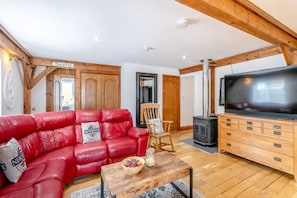 A cozy living room with a red leather sofa, a wooden coffee table, a television, and a fireplace.