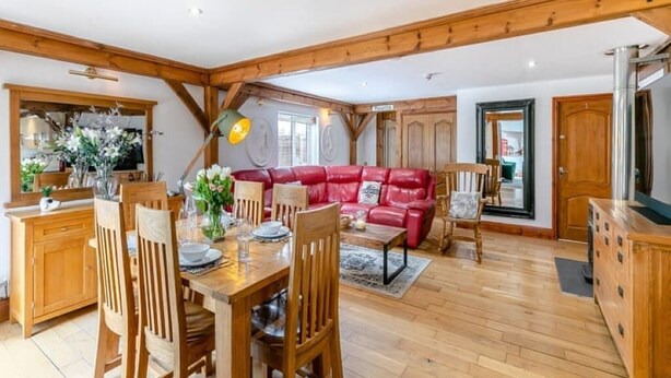 A dining area with wooden furniture, a red leather sofa, and a kitchen area with wooden cabinets.