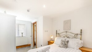 A bedroom with a bed, a nightstand, a wooden wardrobe, a radiator, and a window with blinds.