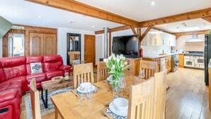 A spacious living area with a red leather sofa, wooden dining table set for four, and a kitchen with wooden cabinets and a stove.