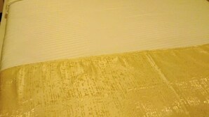 Ein Bett mit weißer Bettdecke und goldfarbener Decke.