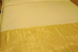 Ein Bett mit weißer Bettdecke und goldfarbener Decke.