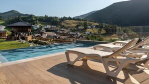 Área de piscina com espreguiçadeiras, deck de madeira e vista para uma aldeia no alto do morro.