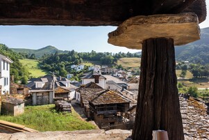 Un pueblo con edificios de piedra tradicionales, un poste de madera destacado y un puente de piedra.