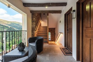 Un balcón con mobiliario de mimbre, una escalera de piedra y una puerta de madera.