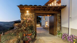 Ein steinerner Bogenbogen führt zu einem Gebäude mit einer Holzpergola und Topfpflanzen.