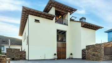 A modern two-story house with a balcony, a stone wall, and a large wooden door.