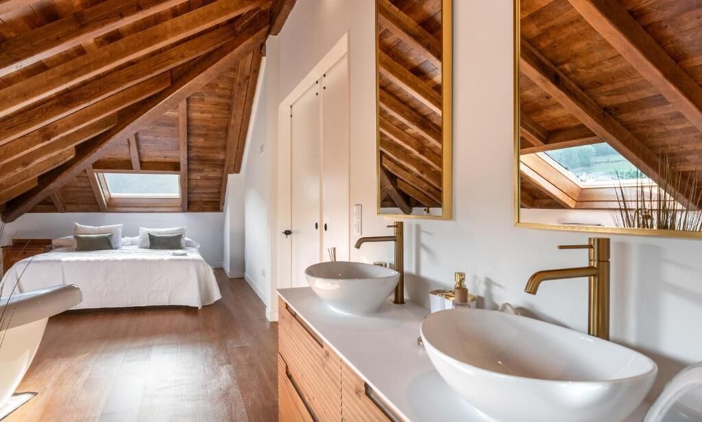 A bedroom with a large bed, a white vanity with a bowl sink, and a skylight.