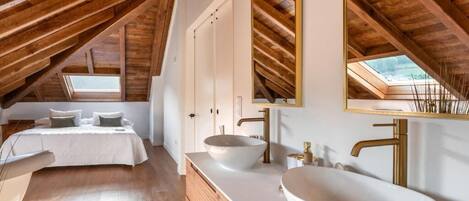 A bedroom with a large bed, a white vanity with a bowl sink, and a skylight.