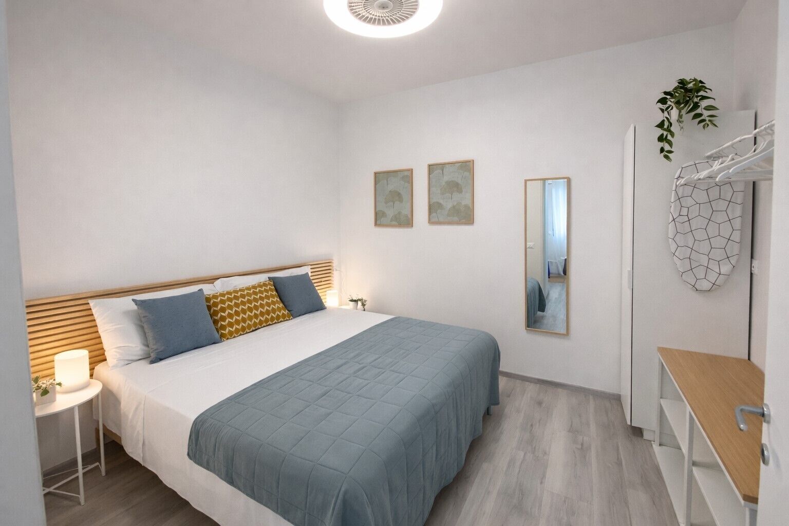 Un dormitorio ordenado con cama, mesita de noche, lámpara y espejo.