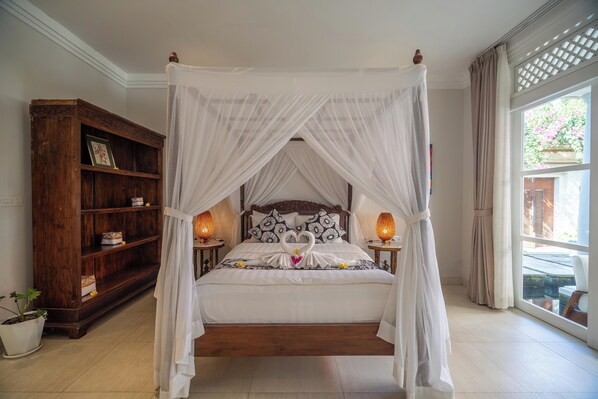 Un letto a baldacchino con tende drappeggiate, cuscini a forma di cigno, una libreria in legno e un'ampia finestra vista su un paesaggio verde.