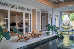 A serene outdoor area with a stone fountain, wooden chairs, and a bed with a canopy. - Raaga Samudra - Luxury 3BR Villa, Private Pool, Ocean View, Near Sandy Beach (Bali)