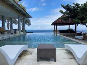 Area piscina con lettini e zona relax coperta con vista sul mare.
