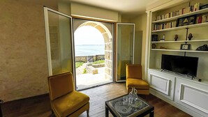 Sala de estar com vista para o mar, uma estante de livros e uma televisão.