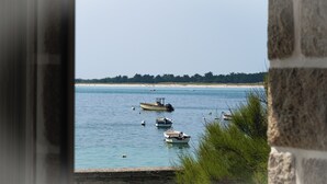 Vista costeira com barcos em águas calmas, uma praia de areia e uma área arborizada ao longe.
