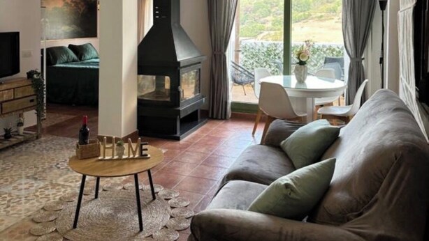 A living room with a fireplace, a sofa, a coffee table, and a view of the outdoors.