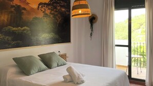 A bedroom with a large bed, a ceiling artwork, a hanging lamp, and a view of greenery outside.