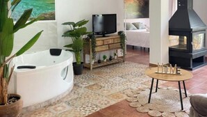 A living room with a TV, a fireplace, a sofa, a coffee table, and a wall with 'OASIS RURAL' text.
