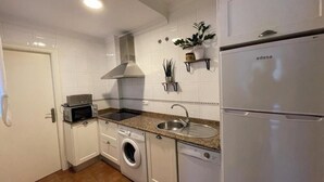 A compact kitchen with white cabinetry, a built-in oven, a microwave, a washing machine, a dishwasher, and a refrigerator.