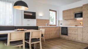 A modern kitchen with wooden cabinetry, a built-in oven, and a dining area with a table and chairs. - Family Apartment with Mountain View, Balcony and Wi-Fi (Campo Tures)