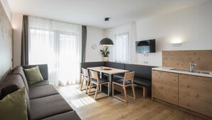 A modern living room with a sofa, dining table, and chairs. There is a kitchen area with a sink and a TV mounted on the wall. - Family Apartment with Mountain View, Balcony and Wi-Fi (Campo Tures)