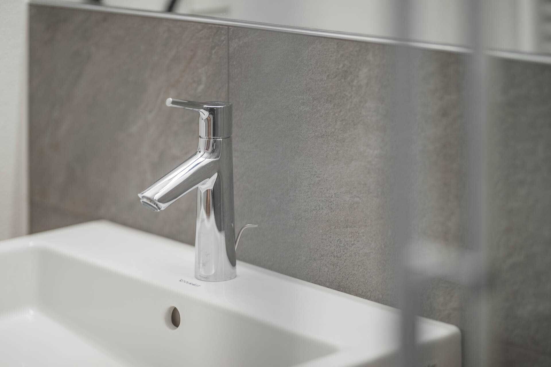 A bathroom sink with a chrome faucet, a mirror, and a tiled wall.