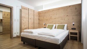 Un dormitorio moderno con cabecera de madera, una cama grande con sábanas blancas, una mesita de noche y un buró de madera.