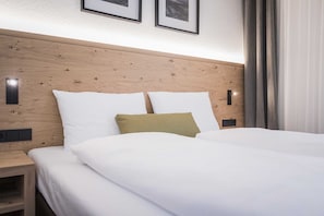 Et hotelværelse med sengegavl i træ, to hvide puder og en grøn pude samt et hvidt sengetæppe.