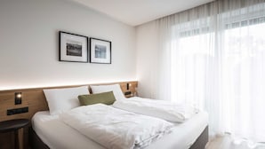 A hotel room with a large bed, a nightstand, a wall-mounted lamp, and a window with sheer curtains. - Studio Apartment 'Superior' with Mountain View, Shared Garden and Wi-Fi (Campo Tures)