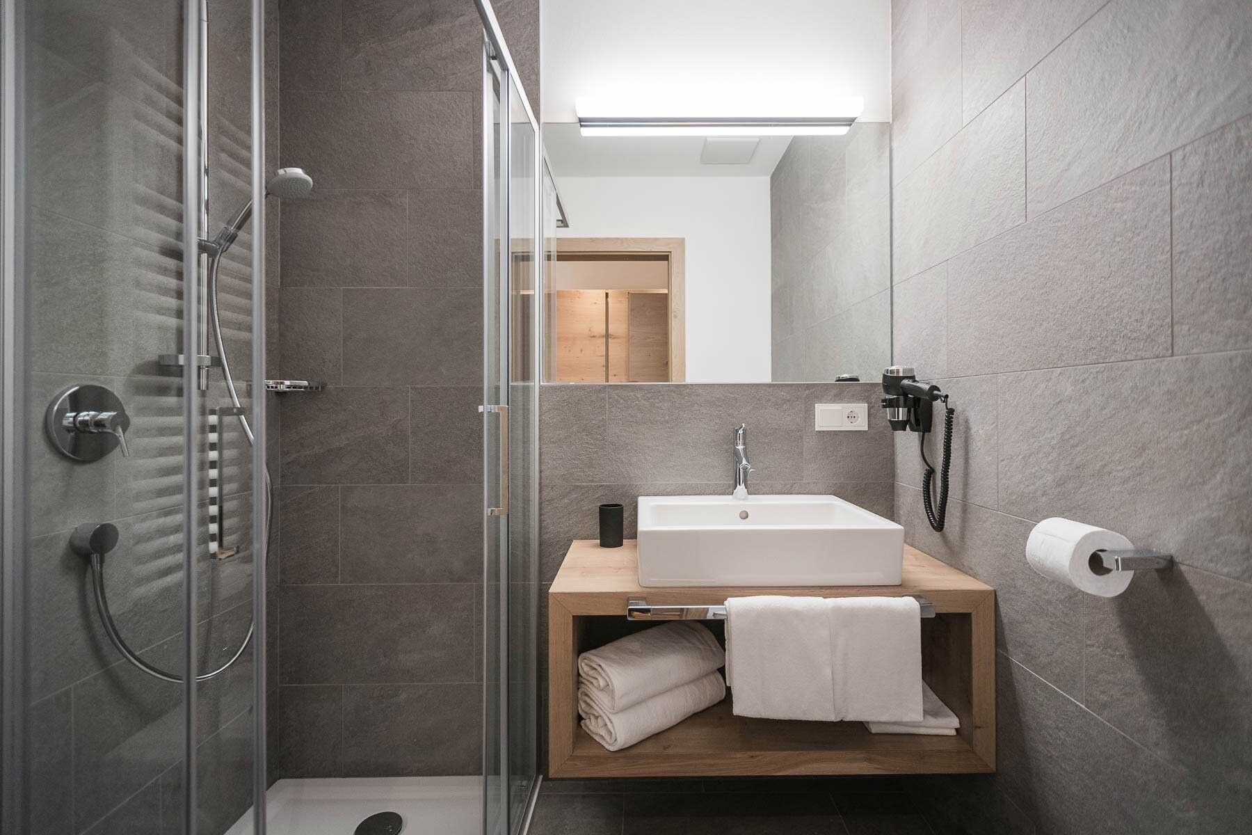 Une salle de bain moderne avec une douche à parois de verre, un meuble-lavabo en bois et un porte-rouleau de papier toilette.