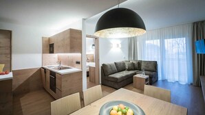 Een moderne keuken met houten kastjes, een eethoek met een tafel en stoelen, een bank en een grote hanglamp.