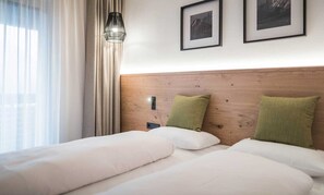 A hotel room with a wooden headboard, two beds with white bedding, a nightstand, a wall-mounted light fixture, and two framed pictures on the wall. - Apartment 'Three-room C1 ca. 65m²' with Garden View, Balcony and Wi-Fi (Campo Tures)