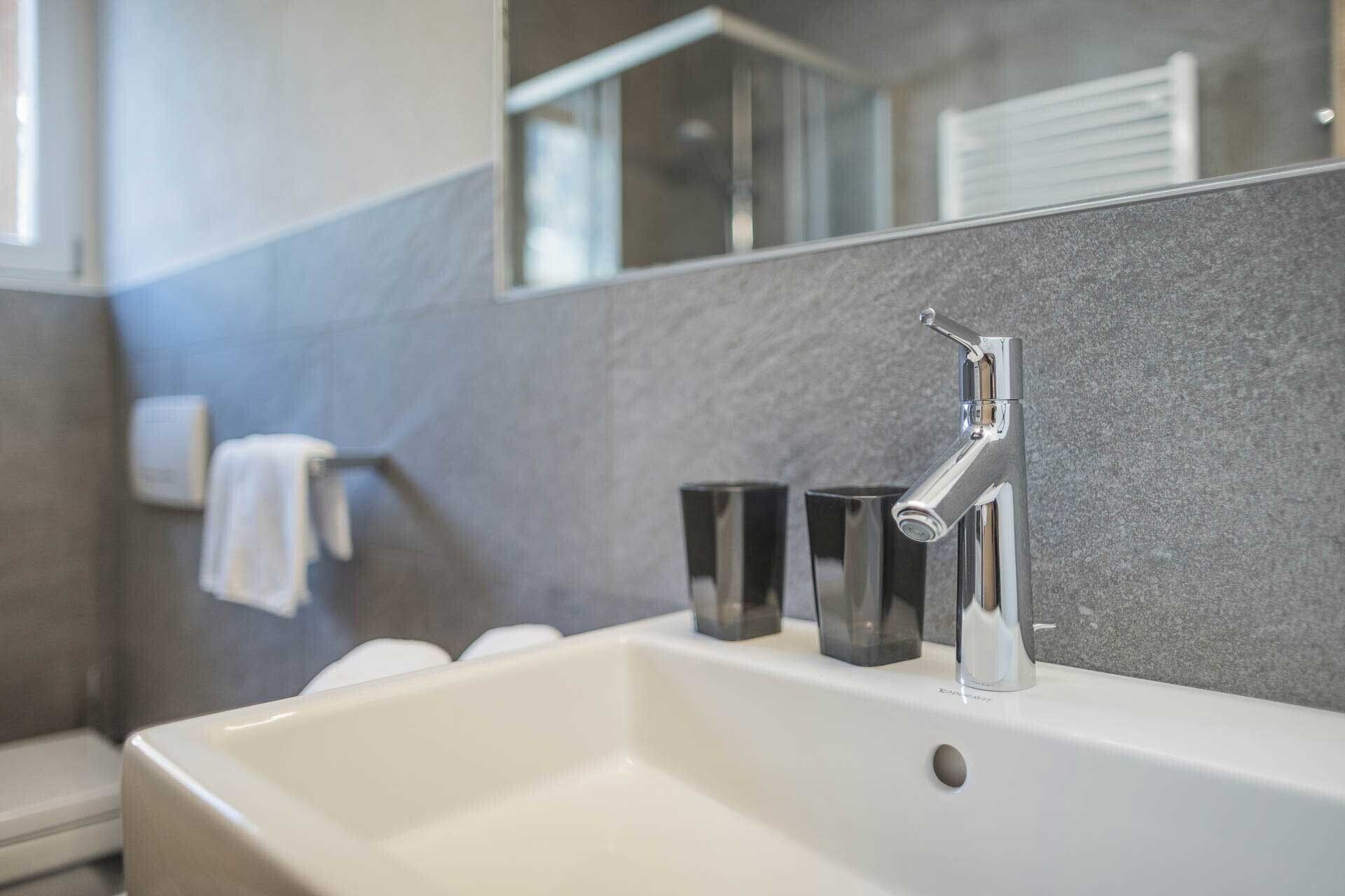Een moderne badkamer met een witte wastafel, een chromen kraan en een grote spiegel.