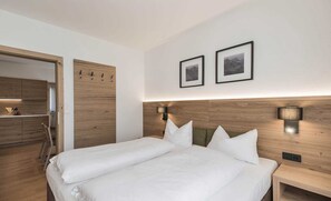 Una habitación de hotel moderna con cabecera de madera, dos lámparas de noche, una cama con ropa blanca y dos cuadros en la pared.
