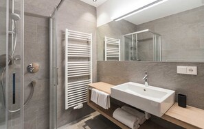 Een moderne badkamer met een douchecabine van glas, een witte wastafel en een handdoekrek.