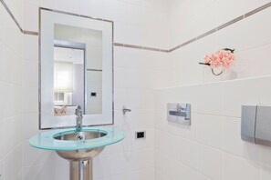 Ein Badezimmer mit einem Waschbecken aus Glas, einem Spiegel, einem Handtuchhalter und einer Blumenkomposition.